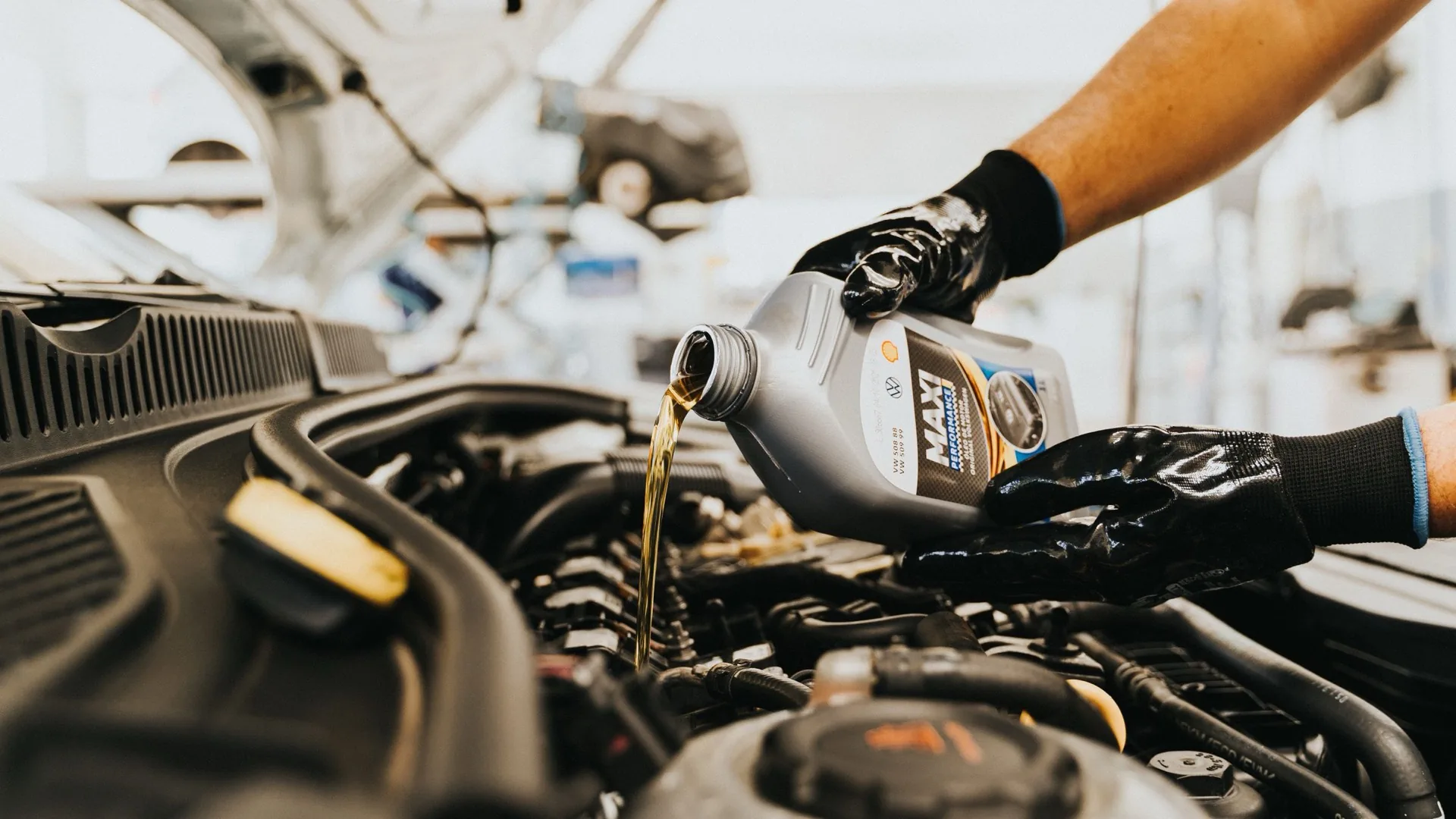 Un mecánico con guantes vierte aceite de un bidón en el motor de un auto.